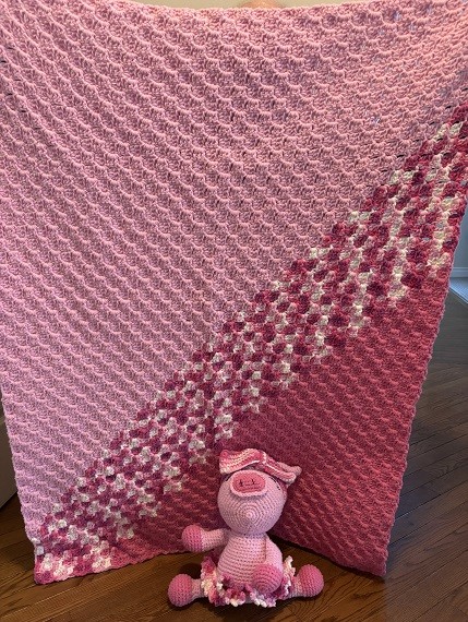 A gradient pink crocheted blanket with a stuffed pig